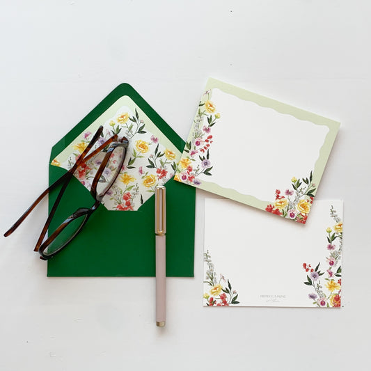 White stationery card with light green scalloped border and bright watercolor garden roses, sweet peas, pansies, peonies and delphinium and kelly green envelope lined with matching watercolor artwork