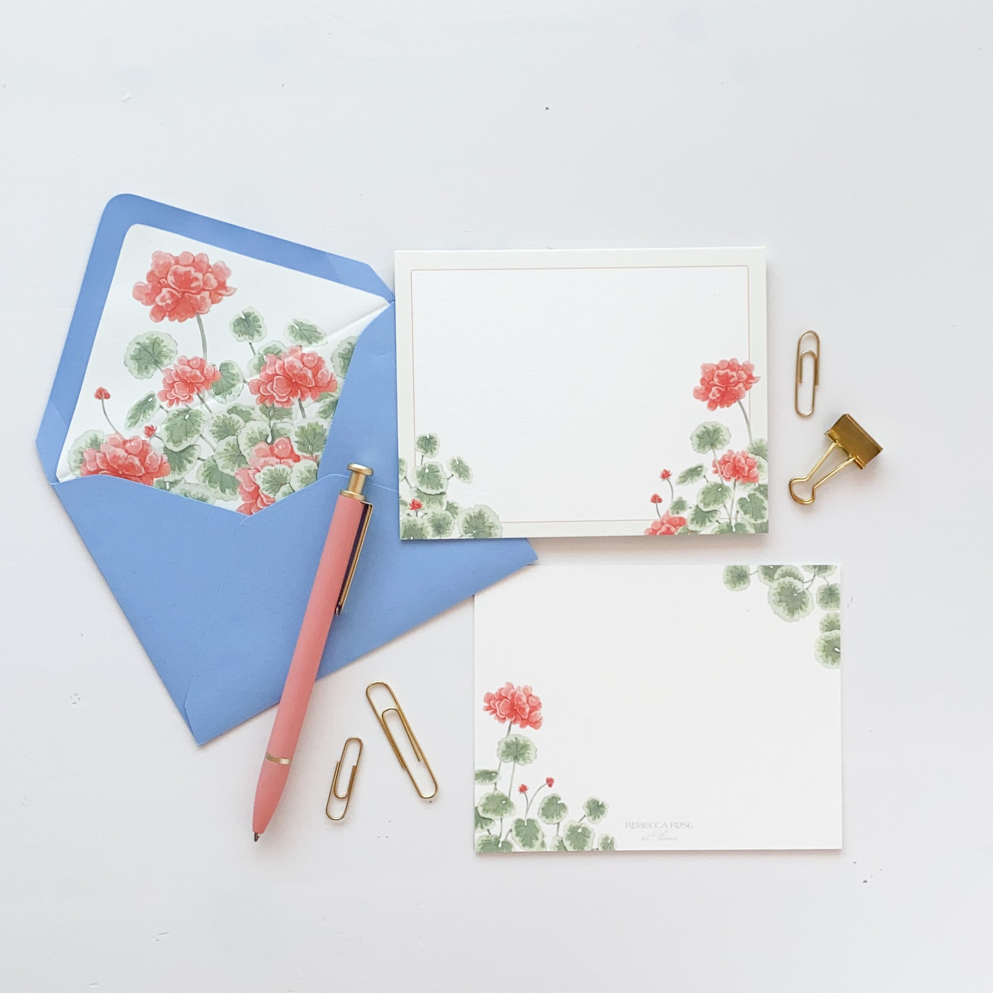 White stationery card featuring red geranium and greenery watercolor artwork. Light blue envelope lined with matching red geranium watercolor artwork.