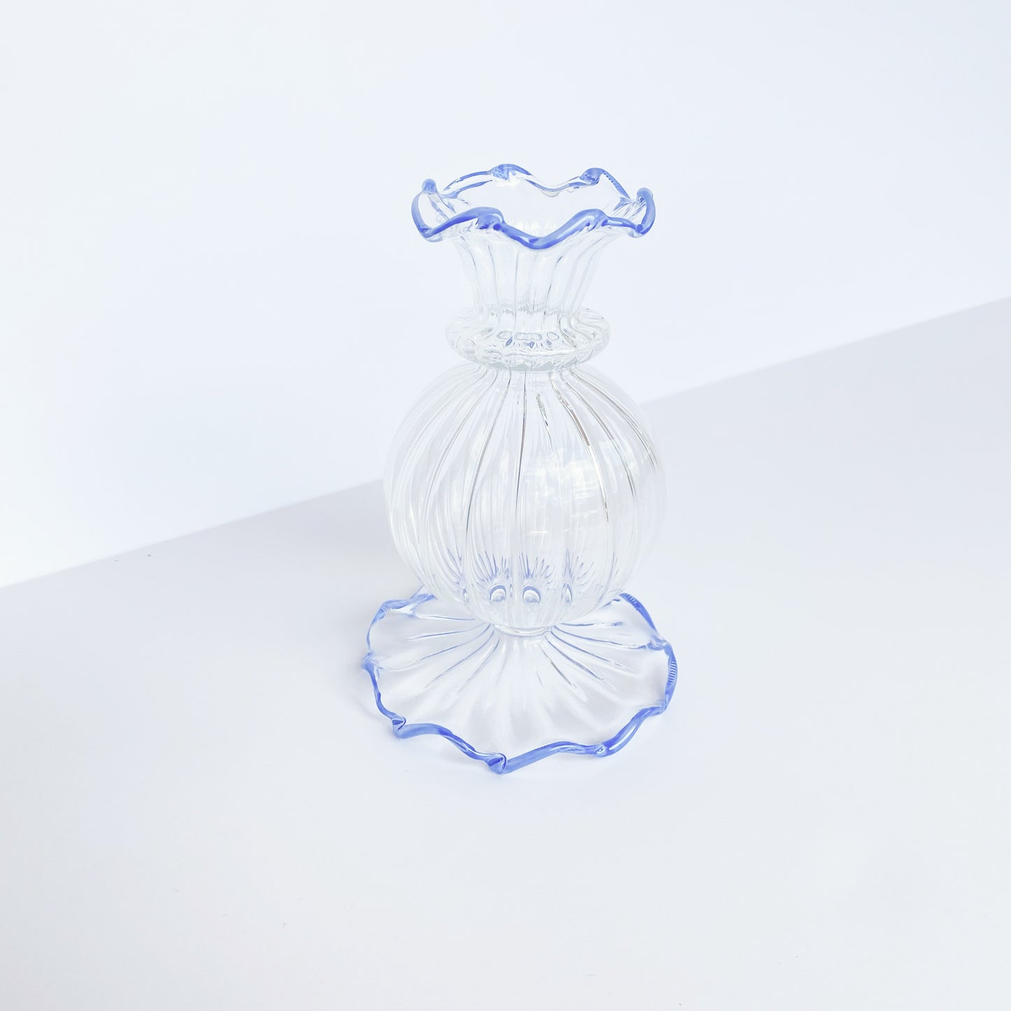 Clear glass bud vase with ruffled blue rim at the top and bottom.