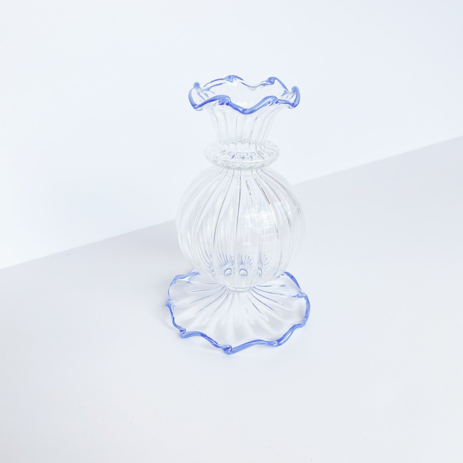 Clear glass bud vase with ruffled blue rim at the top and bottom.