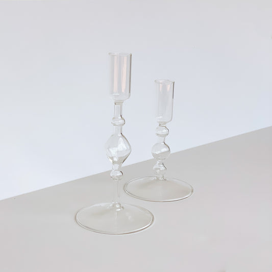 Two delicate clear glass candle holders of varying height with bulb detailing on the stem