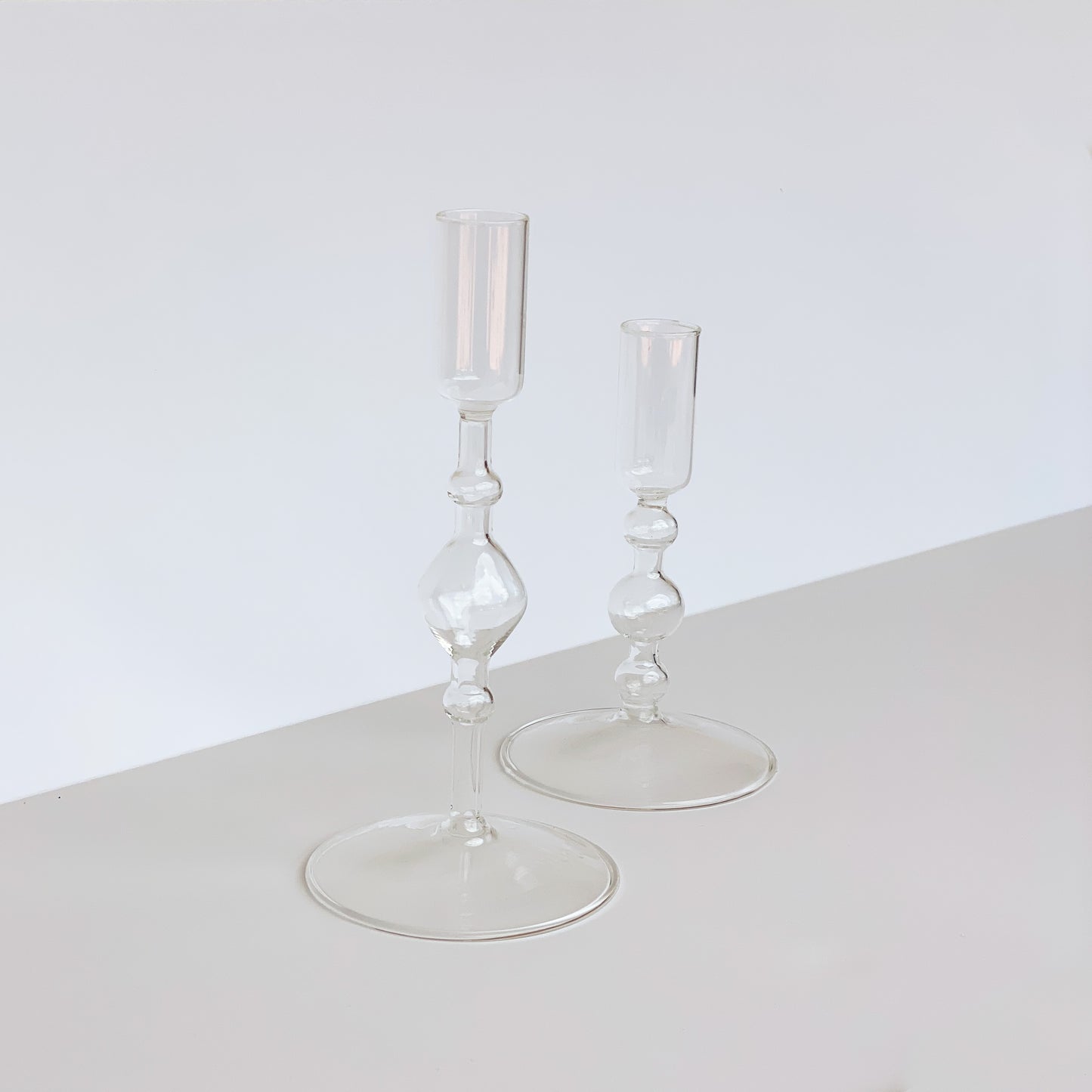 Two delicate clear glass candle holders of varying height with bulb detailing on the stem