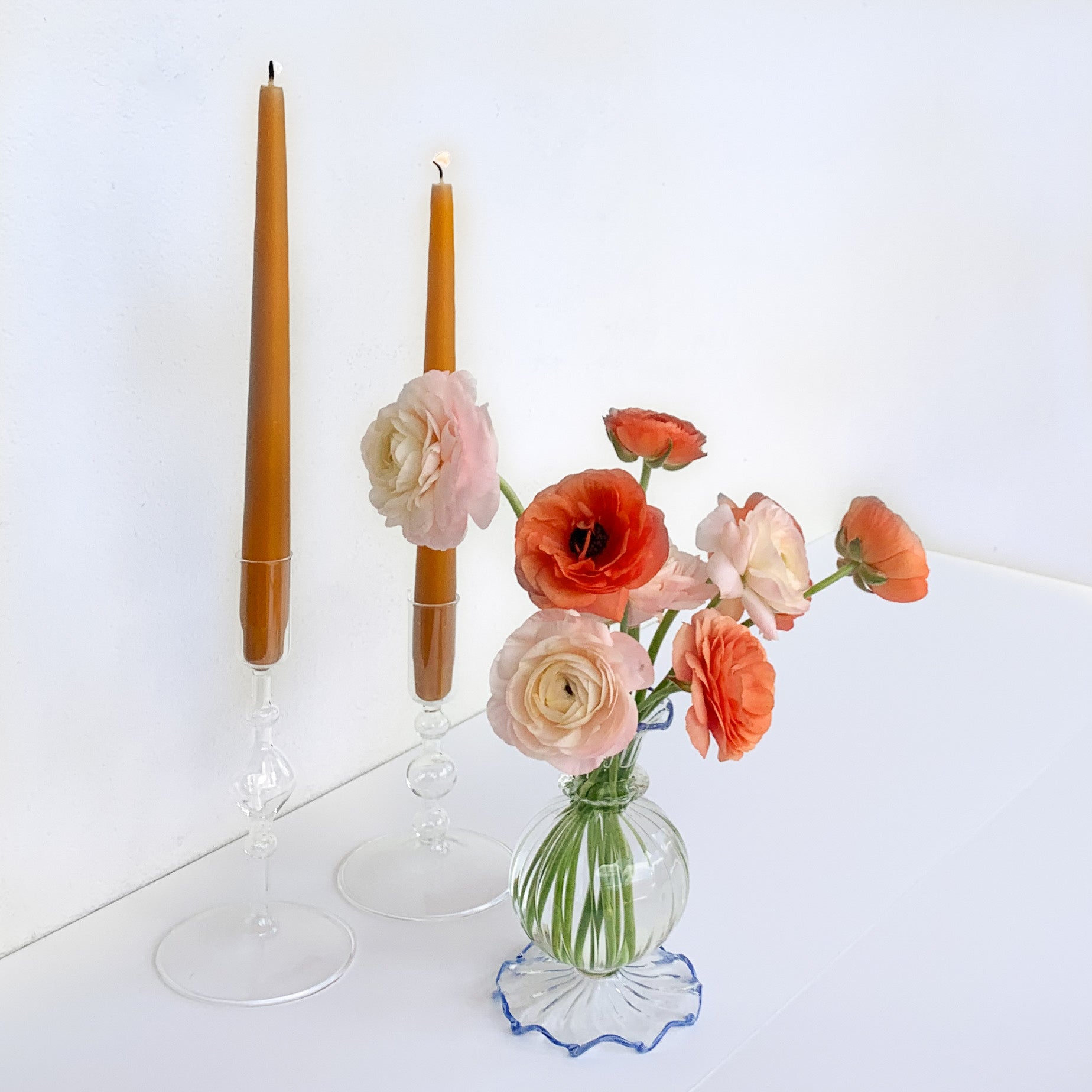 Two clear glass candleholders featuring mustard yellow candles with a clear glass bud vase and blue rim