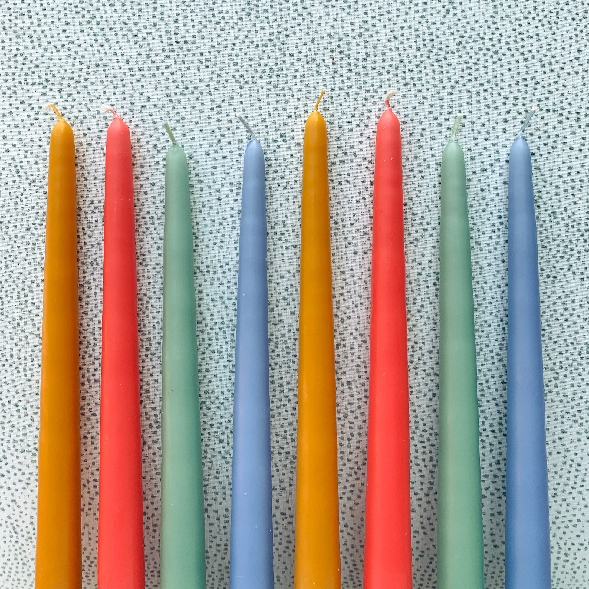 Mustard yellow, bright coral, eucalyptus green and periwinkle taper candles in a line.