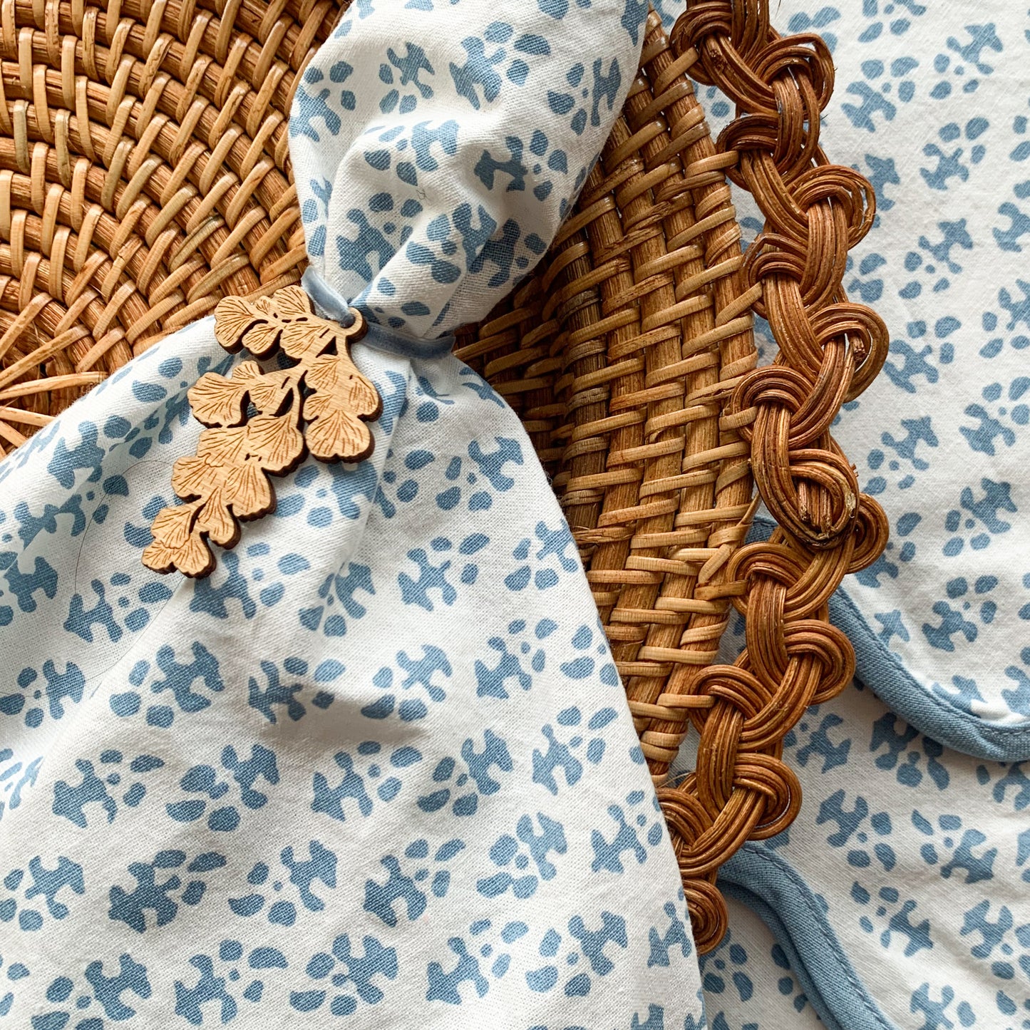 Rattan charger with white and light blue batik patterned cloth napkin with light blue scalloped edge and laser cut maiden hair fern napkin charm.