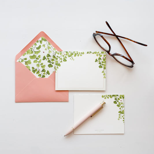 White stationery card featuring a frame of delicate maidenhair fern greenery with ladybugs. Light coral envelope lined with matching maidenhair fern watercolor artwork.
