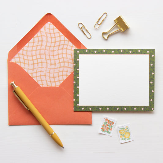 White notecard with olive green and light pink geometric tile patterened border. Terracotta orange envelope lined with a light pink and terracotta wavy checkered pattern.