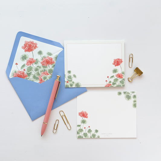 White stationery card featuring red geranium and greenery watercolor artwork. Light blue envelope lined with matching red geranium watercolor artwork.
