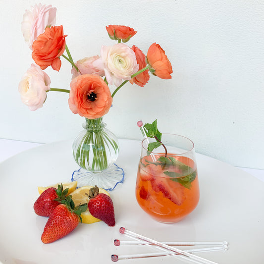 Glass with a strawberry cocktail, mint sprig and acrylic ladybug stir sticks